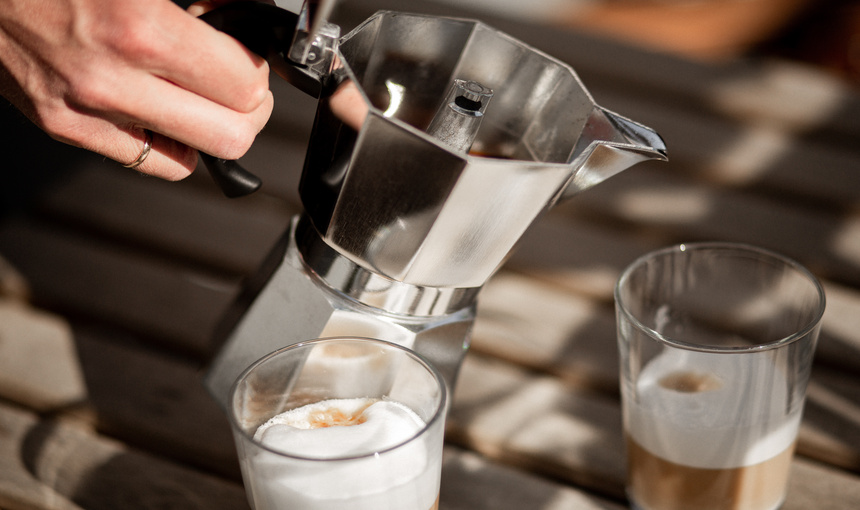 A woman pouring coffee from a moka pot into glasses.